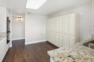 Kitchen featuring light stone counters, dark wood-style flooring, double oven, and white cabinets