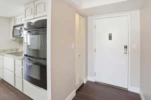 Kitchen featuring black appliances, dark wood-style flooring, white cabinetry, and light stone countertops