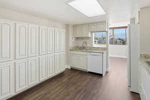 Kitchen with light stone counters, white appliances, and dark wood-type flooring