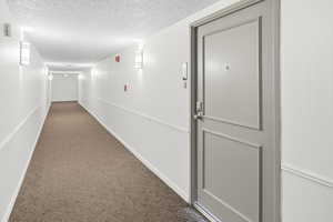 Hallway with dark carpet and a textured ceiling