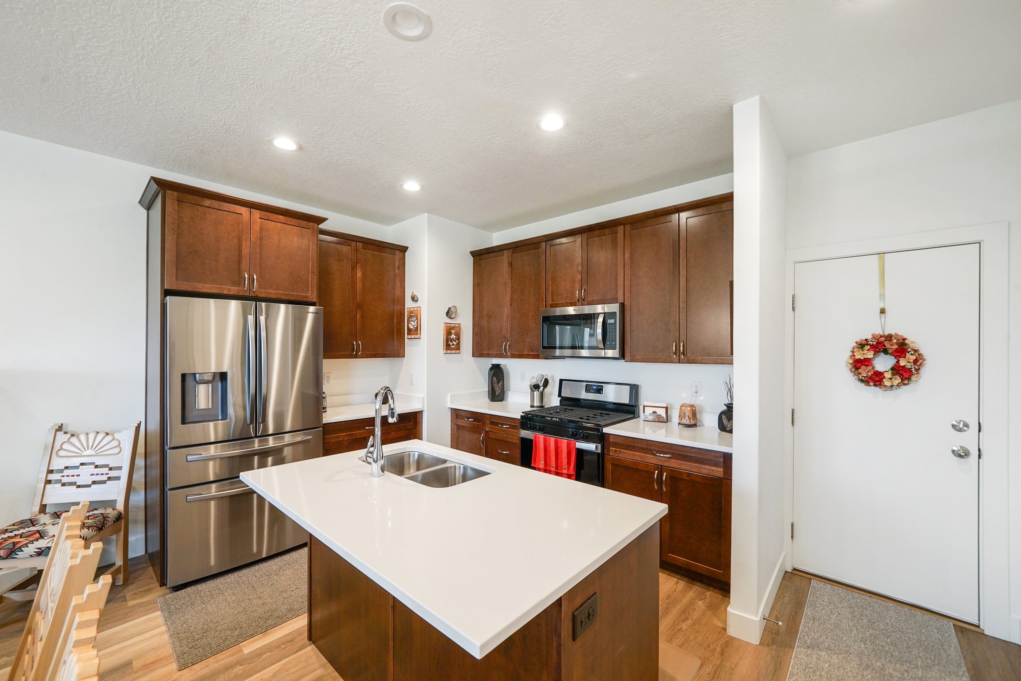 Kitchen with stainless steel appliances, light wood-type flooring, an island with sink, recessed lighting, and light stone countertops