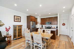 Kitchen with a kitchen island with sink, stainless steel appliances, light wood-style flooring, dark wood finish cabinetry, and recessed lighting