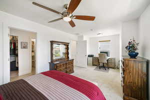 Bedroom featuring a walk in closet, ceiling fan, light carpet, a desk, and a textured ceiling