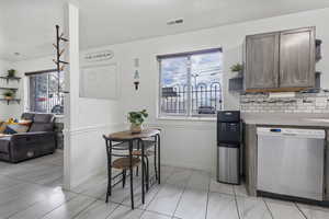 Kitchen with open shelves, stainless steel dishwasher, light countertops, decorative backsplash, and dark wood finish cabinets