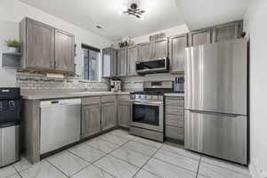 Kitchen with stainless steel appliances, light countertops, open shelves, and backsplash