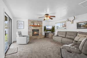 Living area featuring ceiling fan, carpet floors, and a stone fireplace