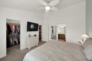 Bedroom featuring a walk in closet, light colored carpet, a ceiling fan, a high ceiling, and ensuite bathroom
