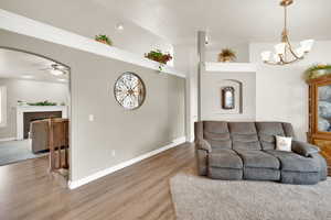 Living area featuring a tiled fireplace, light wood-type flooring, arched walkways, a ceiling fan, and hanging lights