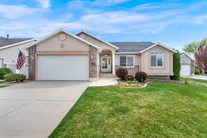 Ranch-style house featuring an attached garage, stucco siding, concrete driveway, a front yard, and brick siding