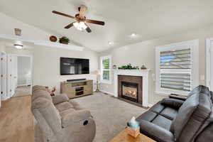 Living room with lofted ceiling, a ceiling fan, a tile fireplace, and light wood finished floors