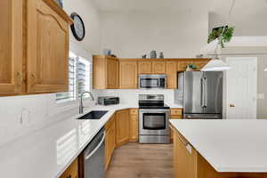 Kitchen with stainless steel appliances, backsplash, light wood-style flooring, hanging light fixtures, and light stone counters