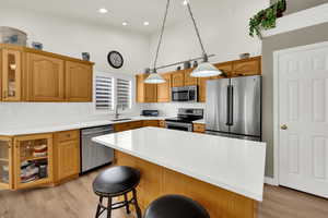Kitchen with stainless steel appliances, glass fronted cabinets, light wood-style flooring, backsplash, and a center island