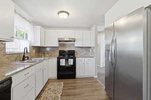 Kitchen with black appliances, white cabinets, light countertops, backsplash, and light wood-type flooring