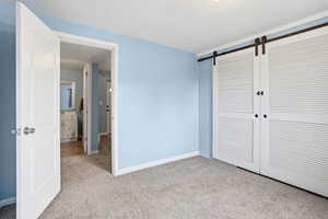 Unfurnished bedroom with a barn door, light carpet, and a closet