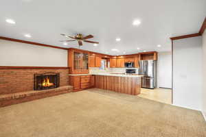 Kitchen with crown molding, ceiling fan, stainless steel appliances, a fireplace, and light countertops