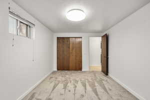 Unfurnished bedroom featuring light carpet, a closet, and a textured ceiling