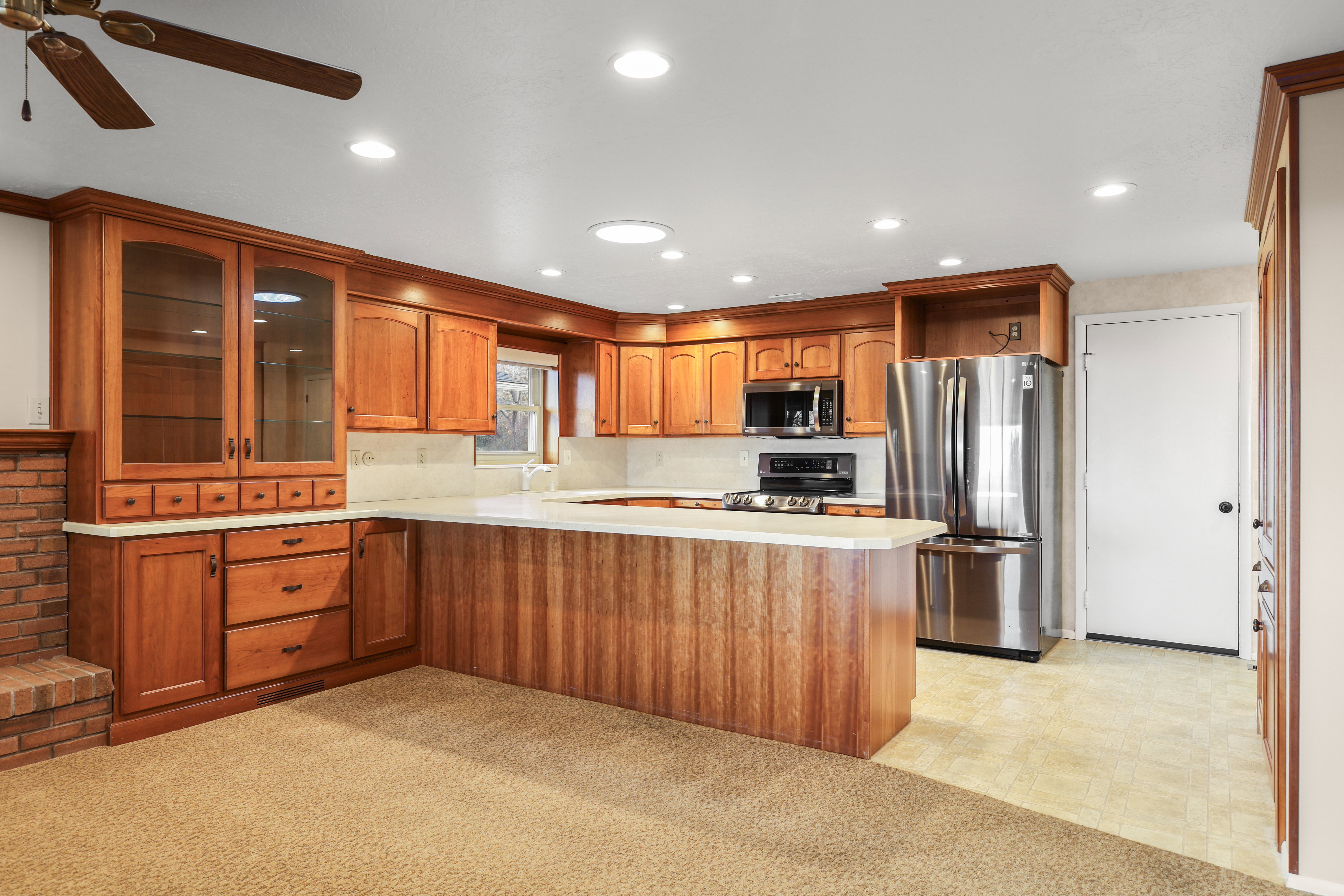 Kitchen with stainless steel appliances, glass insert cabinets, wood finish cabinets, light countertops, and recessed lighting
