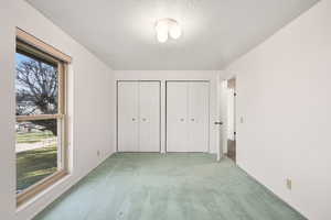 Unfurnished bedroom featuring two closets, light carpet, and a textured ceiling