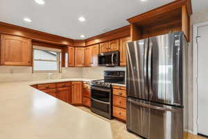 Kitchen with stainless steel appliances, light countertops, light floors, wood finish cabinets, and recessed lighting