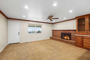 Unfurnished living room with a ceiling fan, a brick fireplace, carpet flooring, recessed lighting, and crown molding