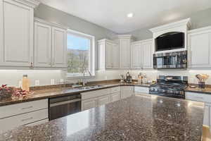 Kitchen featuring dark stone countertops, stainless steel appliances, and white cabinetry