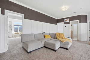 Living room with a decorative wall, wainscoting, crown molding, and carpet floors
