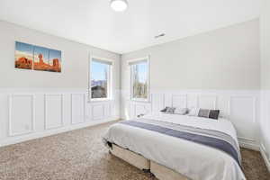 Carpeted bedroom featuring a decorative wall and a wainscoted wall