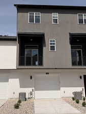 View of back of house with a balcony, a garage, and stucco siding