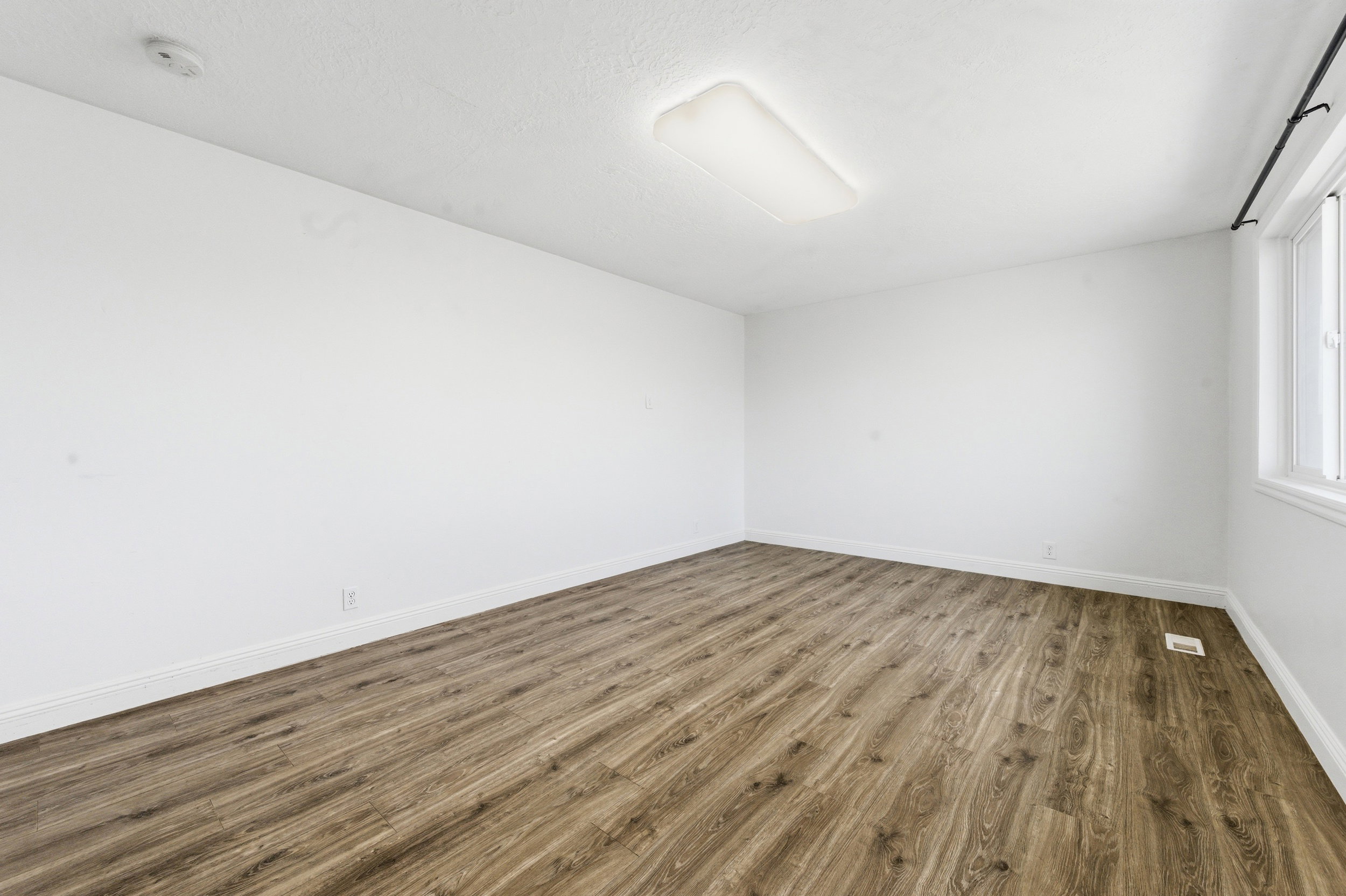 Empty room with dark wood-style flooring and a smoke detector