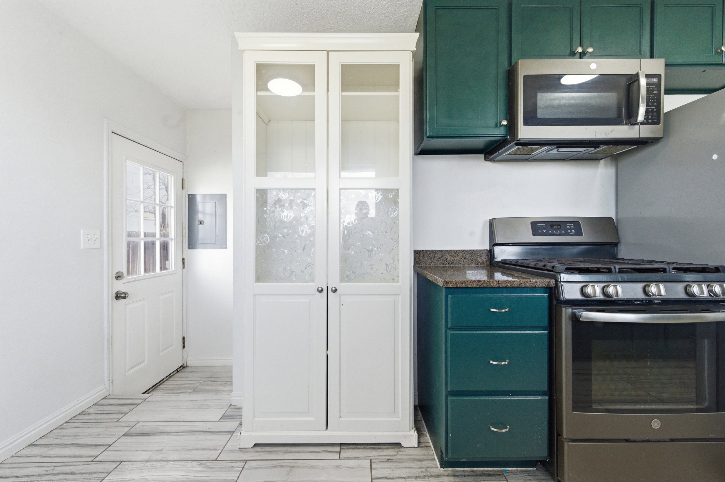 Kitchen featuring stainless steel appliances, green cabinets, electric panel, dark stone counters, and glass fronted cabinets
