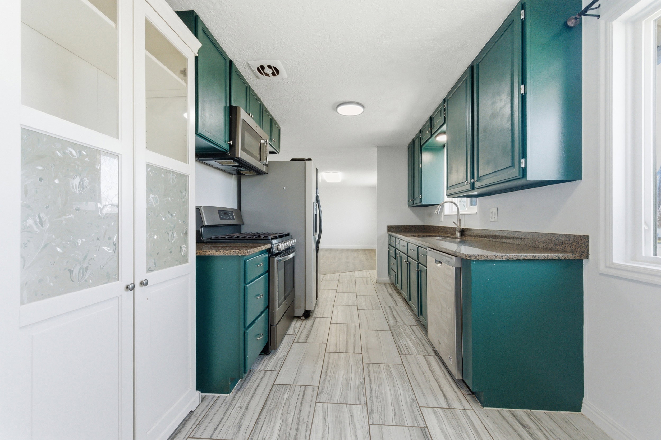 Kitchen with stainless steel appliances, green cabinets, and dark stone counters