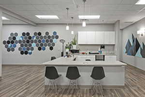 Kitchen with decorative light fixtures, a breakfast bar, a paneled ceiling, white cabinetry, and stainless steel microwave