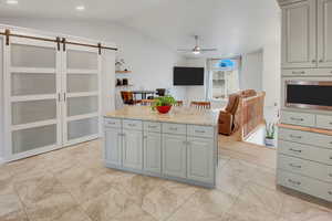 Kitchen featuring a barn door, a ceiling fan, gray cabinetry, open floor plan, and vaulted ceiling