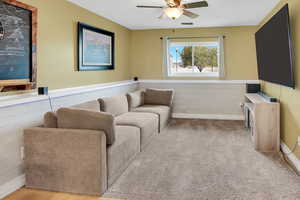 Living area featuring a ceiling fan and a wainscoted wall