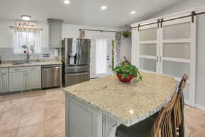 Kitchen with stainless steel appliances, light stone counters, gray cabinetry, a kitchen bar, and recessed lighting