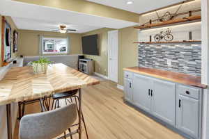 Kitchen featuring butcher block counters, light wood-type flooring, tasteful backsplash, open shelves, and a breakfast bar area