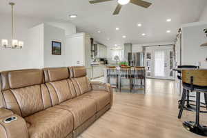 Living room with lofted ceiling, hanging lights, light wood-style flooring, ceiling fan, and french doors