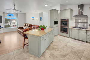 Kitchen with light stone countertops, stainless steel double oven, a breakfast bar area, a ceiling fan, and gray cabinets