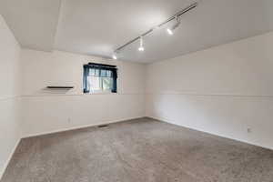 Carpeted empty room featuring rail lighting and baseboards