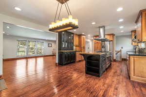 Two tone kitchen with dark stone counters, open shelves, a center island, island range hood, and tasteful backsplash