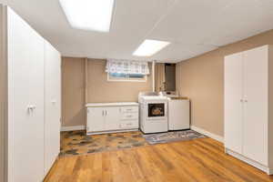Laundry room featuring cabinet space, light wood-style floors, a paneled ceiling, washing machine and clothes dryer, and electric panel