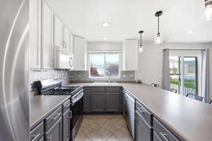 Two tone kitchen featuring stainless steel appliances, two tone cabinetry, light tile patterned floors, a peninsula, and hanging light fixtures