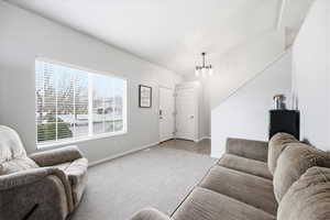 Living room with vaulted ceiling, light colored carpet, and hanging lights