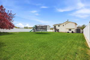Fenced backyard featuring a storage shed, a playground, and a trampoline
