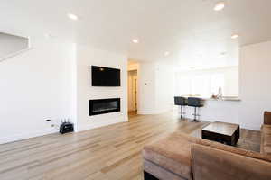 Living area featuring light wood finished floors, a glass covered fireplace, and recessed lighting