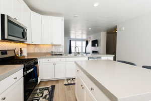 Kitchen with stainless steel appliances, light wood-style floors, a breakfast bar, white cabinets, and a peninsula