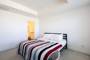 Bedroom featuring light colored carpet, a raised ceiling, and ensuite bath