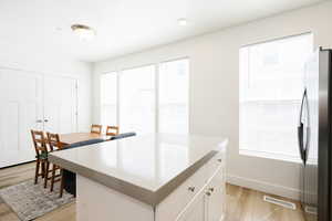 Kitchen featuring a kitchen island, freestanding refrigerator, light wood-style flooring, white cabinetry, and light stone countertops