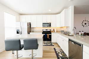 Kitchen with stainless steel appliances, white cabinets, light wood-style floors, a breakfast bar, and a kitchen island