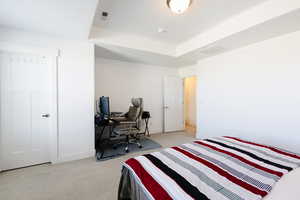 Bedroom featuring an office area, light carpet, and a tray ceiling
